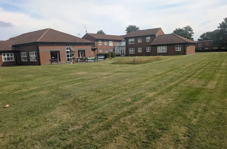Wide communal lawn mown in stripes in front of a brick residential block with benches outside