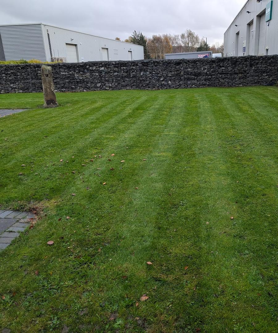 Striped lawn beside a gabion wall at an industrial unit