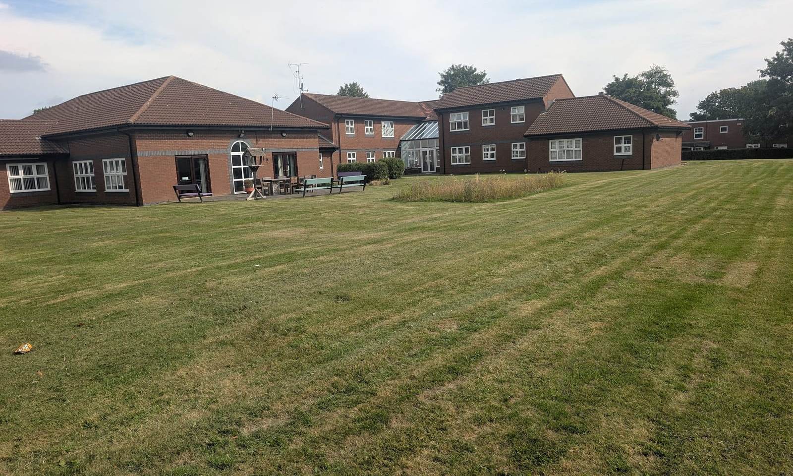 Striped communal lawn in front of low brick buildings and a two storey block