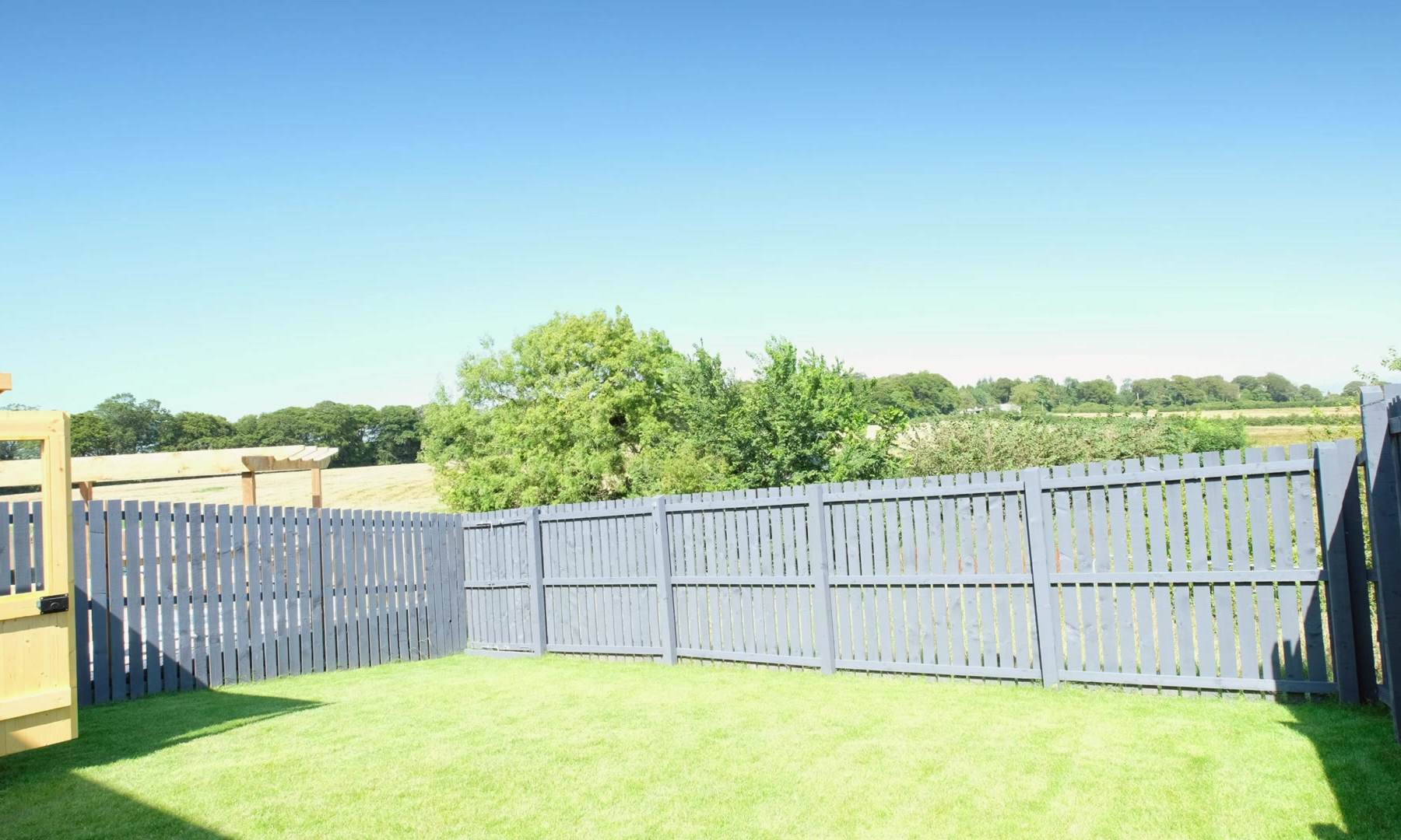 Level new lawn inside a grey painted fence with open countryside beyond