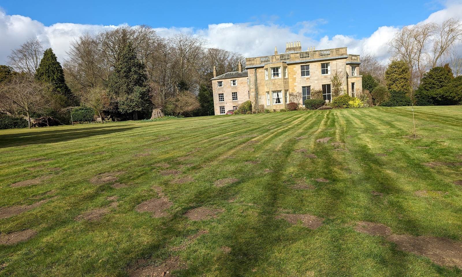 Striped lawn sweeping up to a stone country house under a blue sky