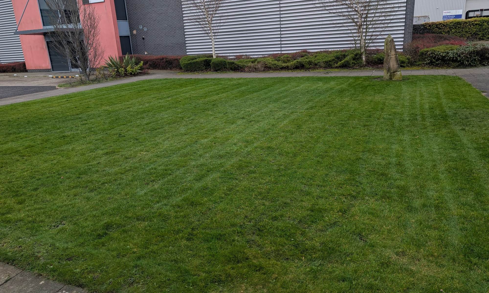 Striped lawn and planted border in front of an industrial unit with a red entrance block