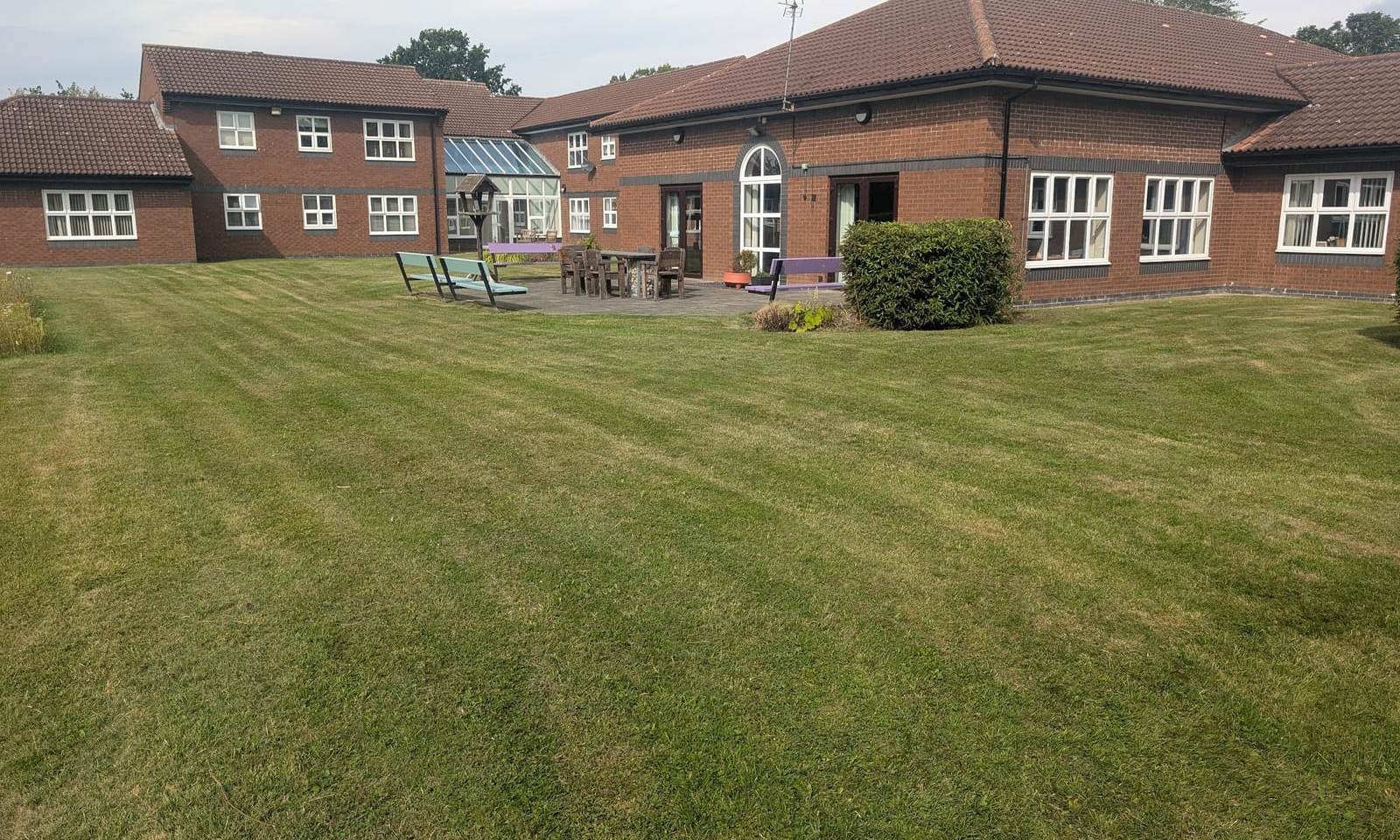 Striped communal lawn in front of a two storey brick building with benches and shrubs