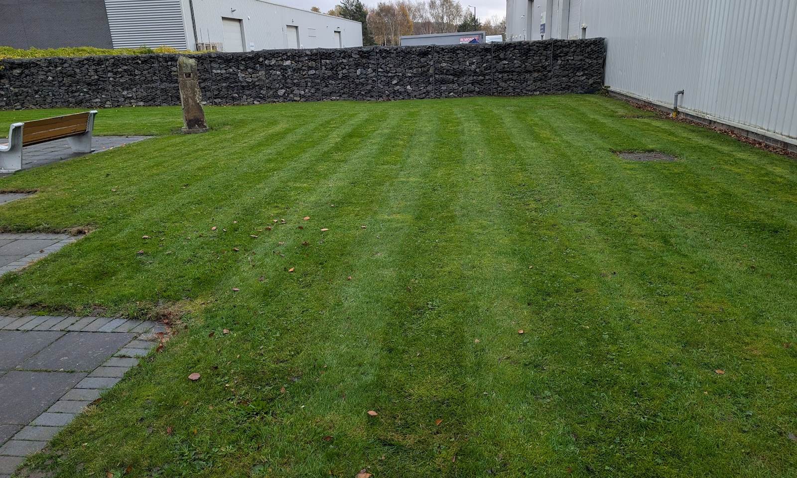Striped lawn beside a gabion wall and a paved path at an industrial unit